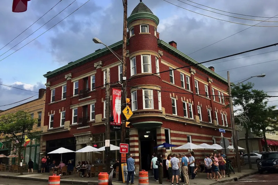 Brick three-story building with restaurant patio umbrellas outside ground floor in Little Italy neighborhood in Cleveland, Ohio.